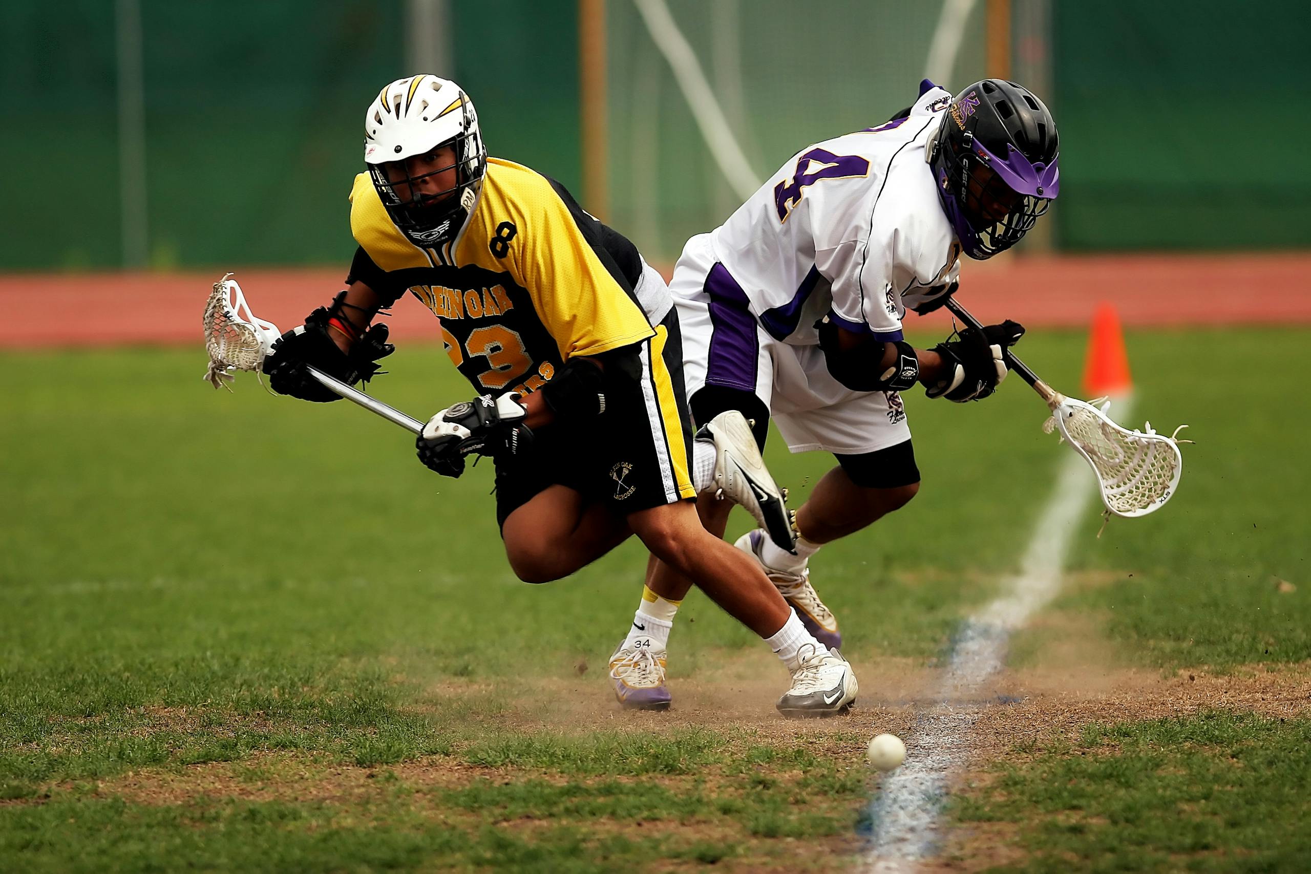 Two men playing an intense lacrosse game outdoors on a grass field.